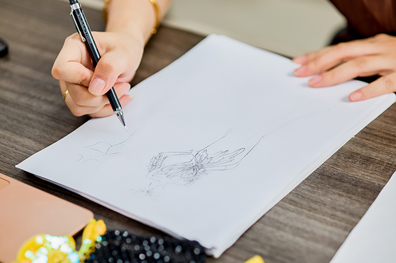 Rysunek projektowy couture wykonany odręcznie na biurku, obok materiały do haftu koralikowego
